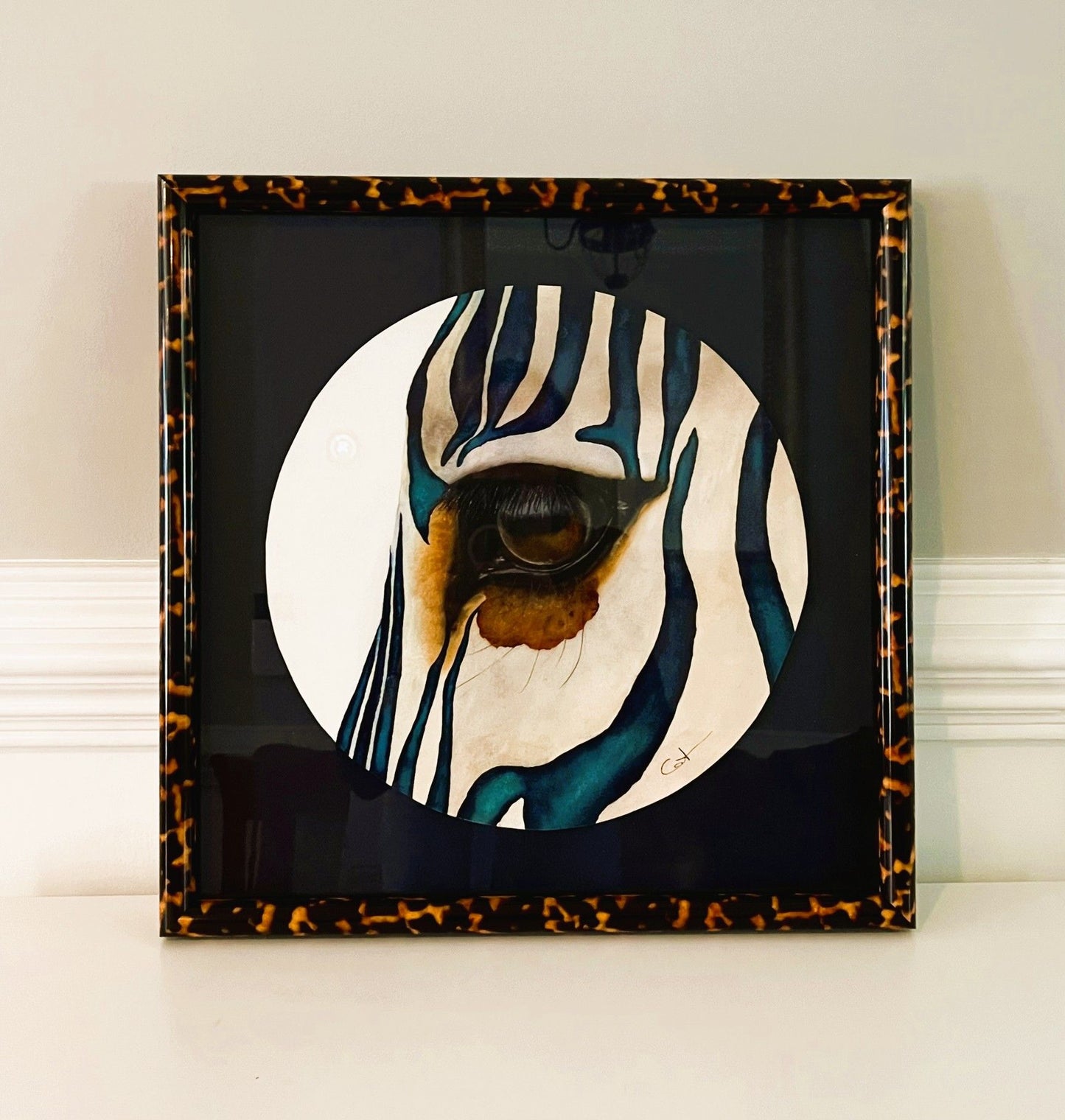 Framed artwork of a zebra's eye with a tortoiseshell border on a white surface.
