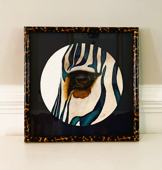 Framed artwork of a zebra's eye with a tortoiseshell border on a white surface.
