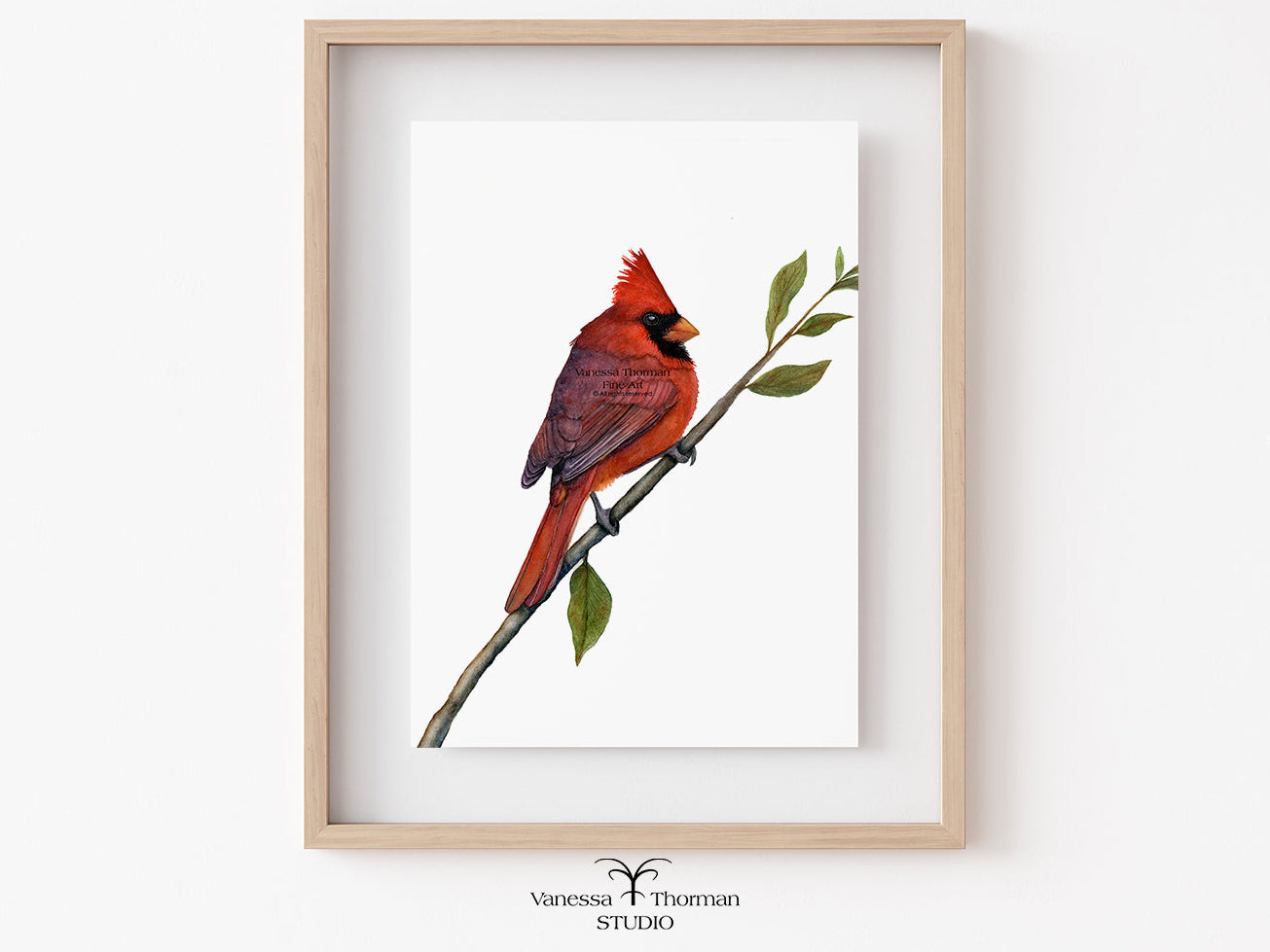 Framed artwork of a red cardinal bird on a branch with leaves, displayed on a white wall.